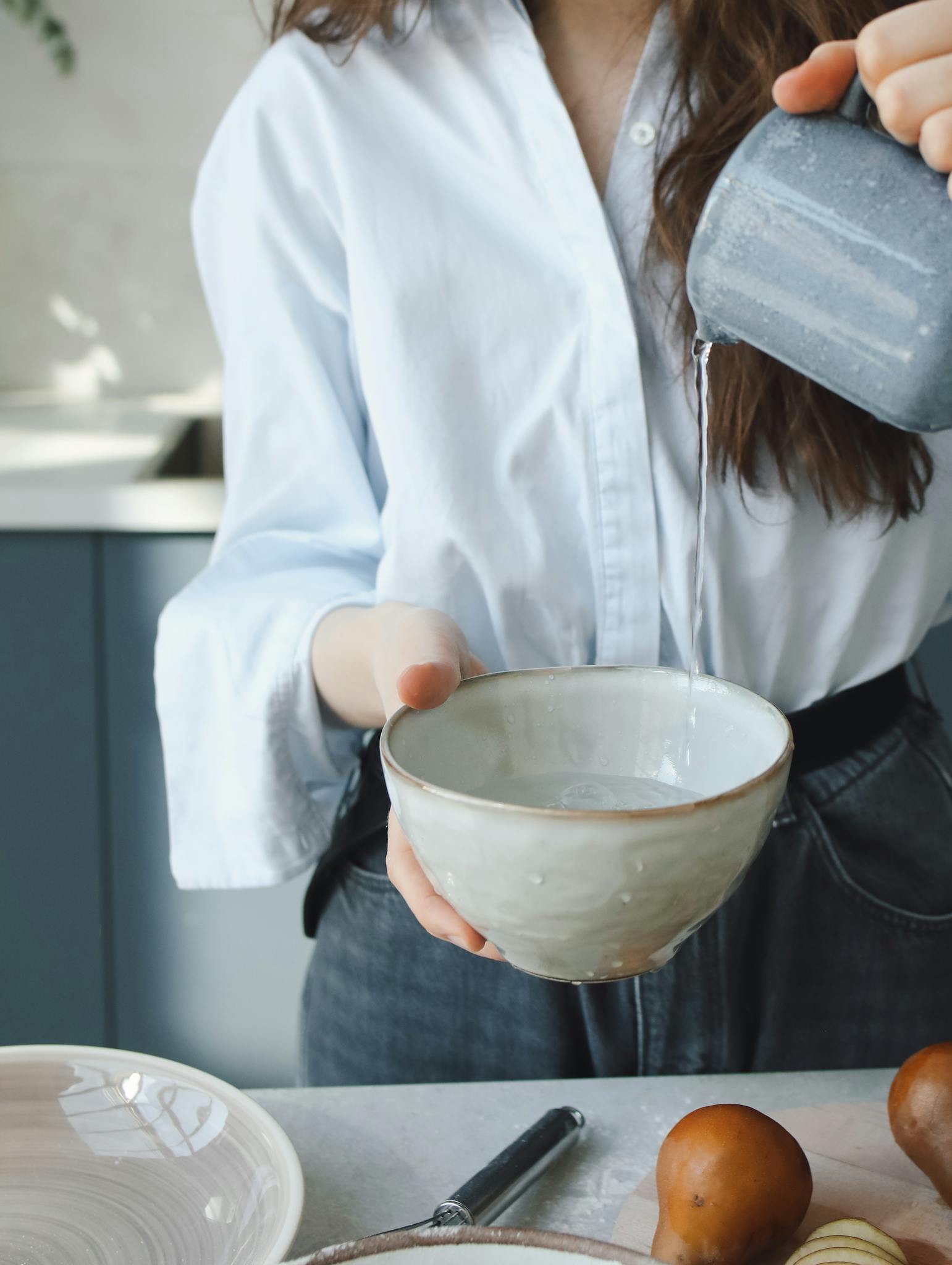 Close-up of a woman pouring water into a bowl in a kitchen setting, focusing on preparation.